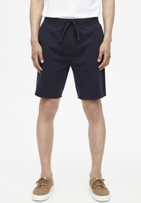 Pantaloni corti blu navy realizzati in tessuto morbido con vita regolabile, caratterizzati da una vestibilità rilassata e una linea dritta, abbinati a scarpe casual marroni.