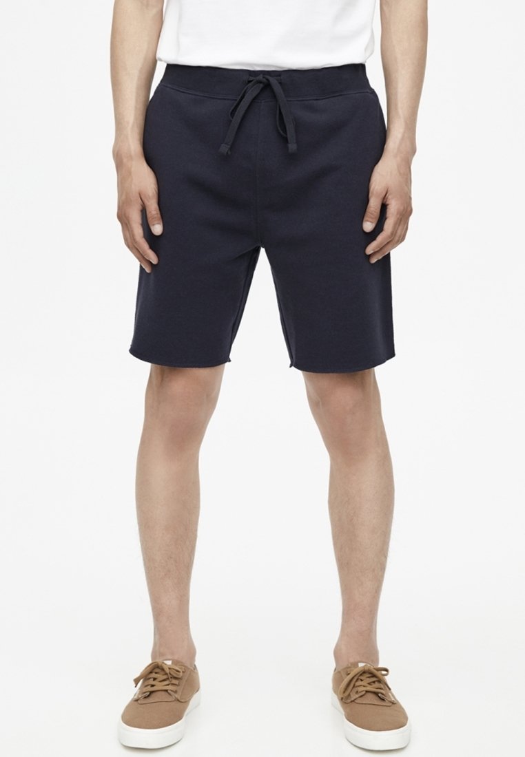 Pantaloni corti blu navy realizzati in tessuto morbido con vita regolabile, caratterizzati da una vestibilità rilassata e una linea dritta, abbinati a scarpe casual marroni.