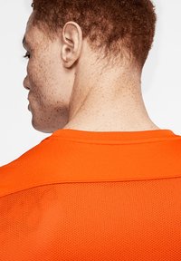 Maglietta sportiva arancione brillante caratterizzata da un design testurizzato e traspirante; tessuto liscio e solido sul colletto e pannelli in rete per ventilazione.