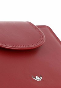 Coin de portefeuille en cuir rouge avec rabat cousu et petit emblème logo argenté sur une surface lisse.