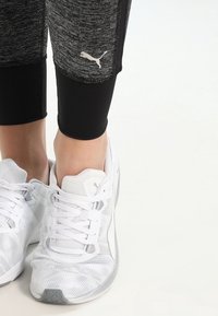 Czarne i szare legginsy sportowe z logo PUMA oraz białe siateczkowe sneakersy z zapięciem na sznurówki i gumową podeszwą.