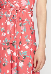 Robe corail avec motif floral en rose, blanc et bleu-vert. Présente une ceinture à la taille et un tissu doux et lisse avec un joli tombé.