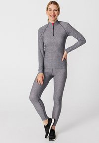 Graues langärmeliges Sportoberteil mit einem Viertel-Reißverschluss und passender, eng anliegender Leggings aus strukturiertem Strickmaterial, kombiniert mit schwarzen Sportschuhen.