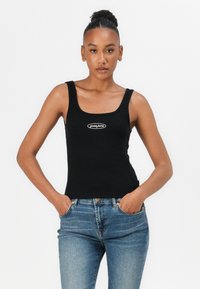 Schwarzes, geripptes Tanktop mit quadratischem Ausschnitt und Logodetail, kombiniert mit blauen, hochgeschnittenen Jeans. Glattes Material, figurbetontes Design.