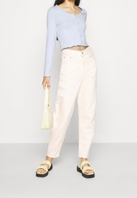 Světle modrý žebrovaný zkrácený kardigan, pastelově růžové džíny s vysokým pasem, žluté sandály s volány a malá žlutá kabelka.