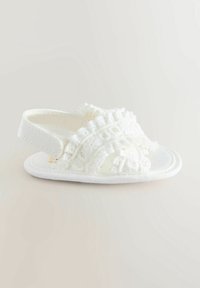 Bílé látkové sandály s pleteným svrchním designem, texturovanými detaily a měkkou podrážkou. Mají nastavitelné zapínání pro bezpečné uchycení.