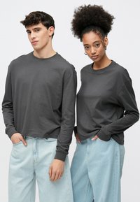 Gray long-sleeve t-shirts with a relaxed fit, combined with light blue denim jeans. Shirts feature round necklines and ribbed cuffs.