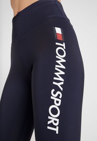 Marina träningsleggings i elastiskt tyg med en vit "TOMMY SPORT"-logotyp och en liten flaggdesign på sidan.
