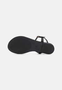 Sandale noire plate avec une semelle en caoutchouc texturé, des fines brides et une boucle ajustable à la cheville pour un maintien sécurisé.