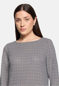 Zwart-wit lange mouwen top met een geometrisch patroon, voorzien van een wijde halslijn en een gladde stoftextuur.