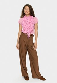 Rozā ruffles blūze ar īsām piedurknēm, slāņota tekstūra; kombinēta ar augsto jostu brūniem platām biksēm, akcentēta ar jostu.