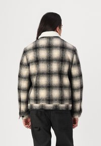 Fleece pamušaluotas, languotas švarkas juodos, grietinėlės ir pilkos spalvų. Turi priekyje užsegamą apykaklę ir struktūrizuotą audinį su ryškiu tinklo raštu.