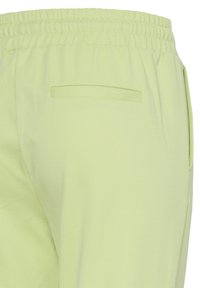 Pantalon vert clair à taille élastique avec une poche passepoilée unique à l'arrière et une poche sur la couture latérale, vu de l'arrière côté droit.