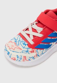 Baskets pour enfants avec des sangles rouges, des lacets blancs, des rayures bleues et une zone de bout blanche à motifs de requins en dessin animé rouges et bleus.