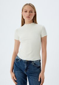 Top corto bianco a coste con scollatura ondulata, design aderente, abbinato a jeans blu di denim. Tessuto semplice e liscio.