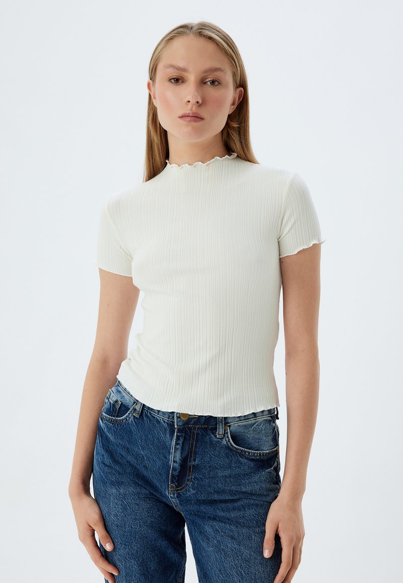 Top corto bianco a coste con scollatura ondulata, design aderente, abbinato a jeans blu di denim. Tessuto semplice e liscio.