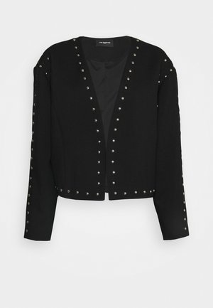 Veste noire courte avec des clous argentés le long des bords, des manches et de l'ourlet, dotée d'un col sans col et d'un design à ouverture frontale.