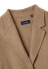 Cappotto in misto lana marrone con colletto a risvolto e spalle strutturate. L'etichetta reca la scritta "PIOMBO" e sono visibili le etichette di cura. Texture morbida.