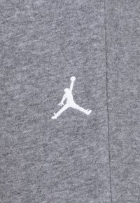 Pelēks audums ar teksturētu rakstu, kur kreisajā pusē ir izteikts balts Jumpman logo.