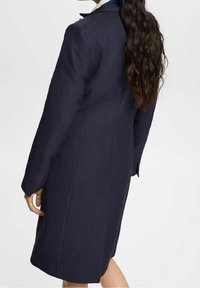 Cappotto lungo blu navy in tessuto testurizzato, con colletto a rever stretto e design sartoriale. Caratterizzato da maniche lunghe e silhouette dritta.