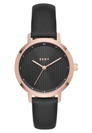 Zegarek z okrągłą kopertą w kolorze różowego złota, czarną teksturowaną tarczą, wskazówkami w kolorze różowego złota, kropkowymi indeksami godzin, czarnym paskiem ze skóry oraz logo DKNY na godzinie 12.