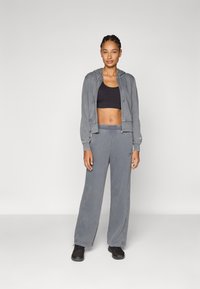 Hoodie gris zippé avec cordons de serrage, associé à un crop top noir et un pantalon de survêtement gris. Texture lisse, coupe décontractée et accents de logo.