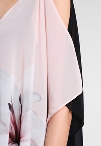 Tessuto trasparente rosa chiaro con una grande stampa floreale bianca e rosa, drappeggiato su una spalla nuda con un tessuto nero sottostante.