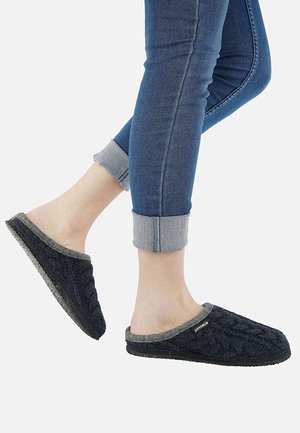 Dark blue knit slippers with a textured pattern, grey fabric lining, and a black sole. Worn with rolled-up blue jeans.