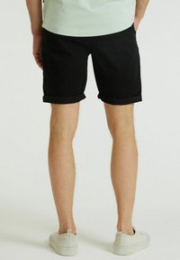 Shorts neri con risvolto, realizzati in tessuto morbido, caratterizzati da una linea dritta e una superficie liscia, abbinati a sneakers chiare.