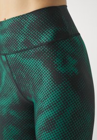 Høytlivs leggings i et grønt og svart prikkete mønster, med en glatt tekstur og elastisk midjebånd for en tettsittende passform.