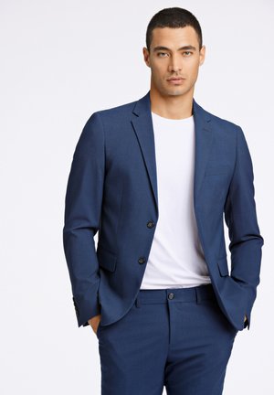 Marineblauer Anzug mit taillierter Passform, zwei Knöpfen und Reverskragen, kombiniert mit einem weißen T-Shirt. Glatter Stoff mit seitlichen Taschen.