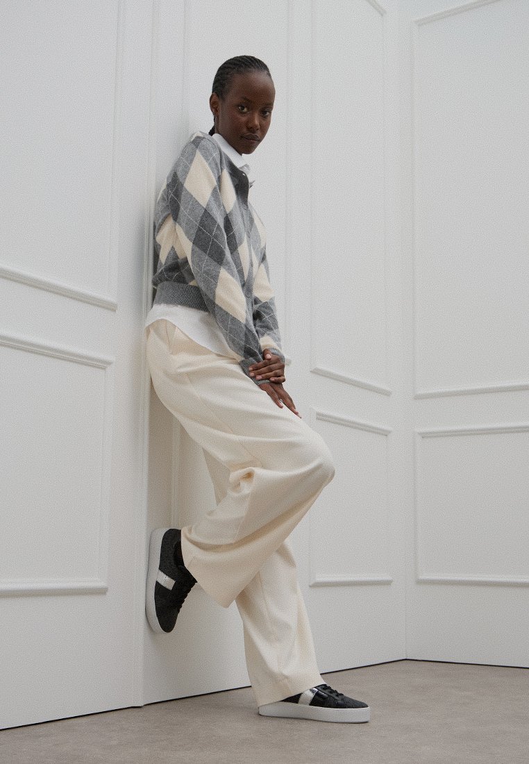 Pareja de pantalones anchos color crema con un suéter en rombos gris y crema. Presentados con zapatillas negras con acentos blancos. Fondo neutro.