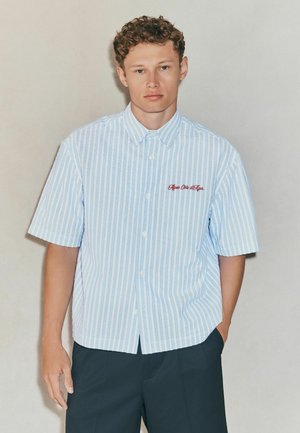 Short-sleeve button-up shirt with light blue and white stripes, featuring red embroidered text on the left chest. Tailored fit and soft fabric.