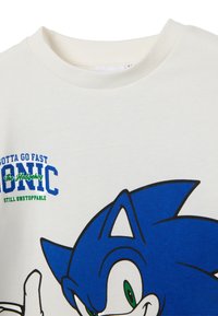 Camiseta de algodón blanca con un gran gráfico azul de Sonic the Hedgehog con contornos negros y texto que dice "Gotta Go Fast" y "Still Unstoppable."