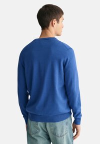 Pullover blu realizzato in tessuto morbido, con scollatura a girocollo, maniche lunghe e polsini e orlo a costine, mostrato da dietro.