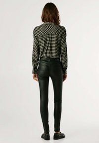 Camisa de cuadros en blanco y negro con mangas largas y diseño de botones, combinada con pantalones de cuero negro ajustados y zapatos negros.