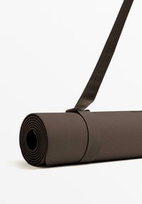 Barna jógaszőnyeg feltekerve, texturált felülettel, és egy hozzá illő pánttal rögzítve, amely megkönnyíti a szállítást.