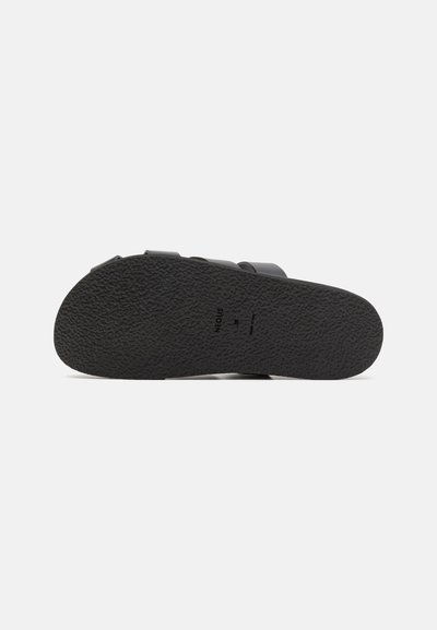Semelle de sandale en caoutchouc noir avec grip texturé, présentant un design minimaliste et une marque subtile. Pas d'accents ni de motifs supplémentaires.