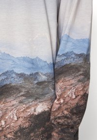 Langärmliges Shirt mit einem Landschaftsdruck, der blaue Gebirgszüge und erdige Texturen zeigt. Weicher Stoff mit einem Farbverlauf-Design.