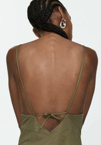 Olivově zelené šaty s nízkým výstřihem na zádech, tenkými ramínky a mašlí v pase. Hladká textura, minimalistický design.