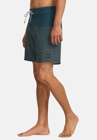 Herren-Swimtrunks in Türkis mit horizontalen senfgelben Streifen. Hergestellt aus leichtem Stoff, mit einem Kordelzugbund und einem runden Logo.