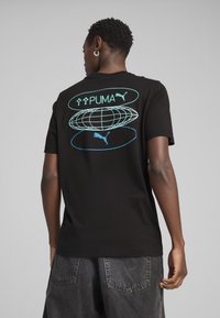 Sort kortærmet t-shirt med en stor blå grafik med "PUMA" tekst og globusdesign på ryggen. Fremstillet af blødt bomuldsstof.