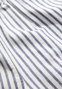 Gros plan d'un tissu blanc avec de fines rayures verticales bleues espacées uniformément et des coutures visibles le long d'une couture.