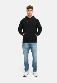 Svart fleecehettegenser med frontlomme og snor. Kombinert med lyseblå jeans og hvite joggesko.