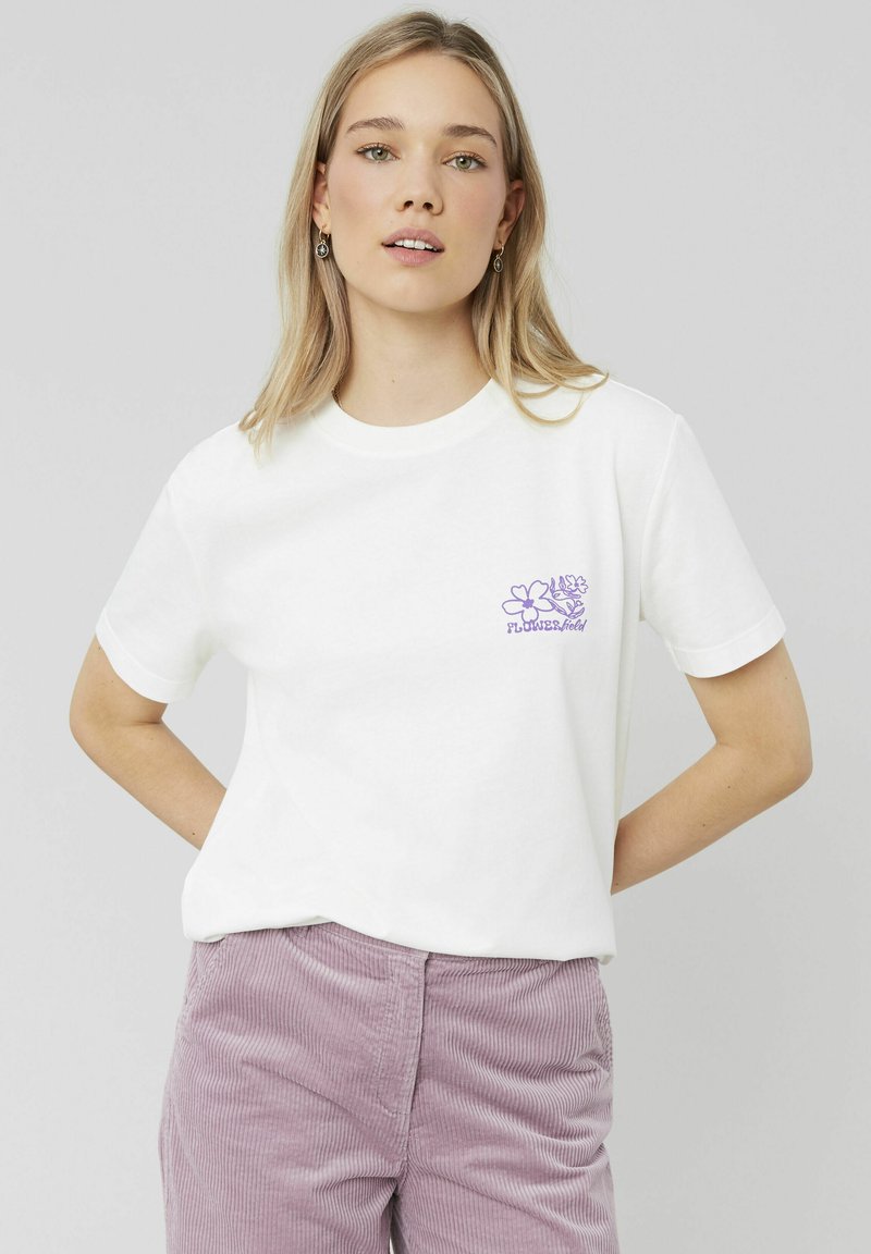 T-shirt en coton blanc avec un motif floral violet sur la poitrine gauche. Manches courtes, col rond et coupe décontractée.