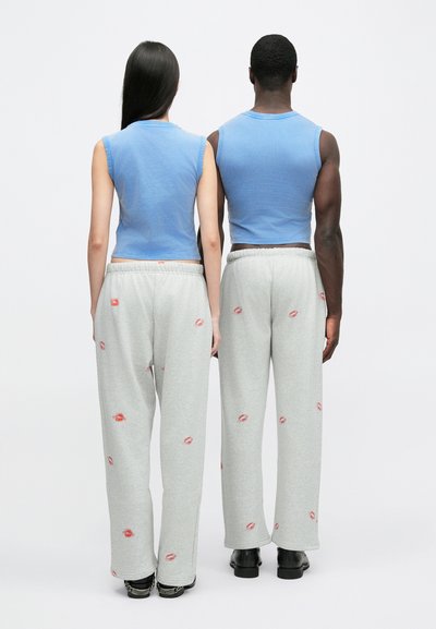 Tops azuis claros sem mangas e calças de treino cinzentas, com detalhes de estampas de lábios vermelhos, em dois modelos de costas contra um fundo neutro.