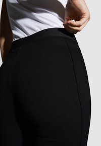 Schwarze, hochtaillierte Hose aus einem glatten, elastischen Stoff. Sie verfügt über einen breiten Bund und Seitennahtdetails, die eine figurbetonte Silhouette erzeugen.