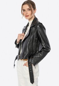 Schwarze Leder-Motorradjacke mit asymmetrischem Reißverschluss, Reißverschlusstaschen, Schulterklappen und einer kurzen Passform. Getragen über einem weißen Oberteil.