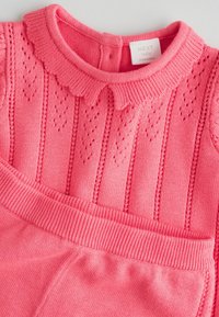 Rózsaszín kötött baba ruha fodros gallérral, texturált mintával és bordázott mandzsettákkal, beépített derékbőséggel a megfelelő illeszkedés érdekében.