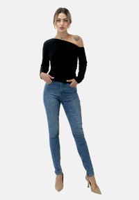 Zwart off-shoulder lange mouw top gecombineerd met lichtblauwe skinny jeans en beige puntige hakken, wat een getailleerd silhouet laat zien.